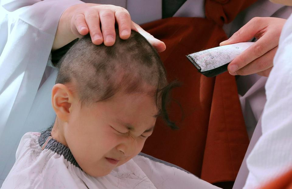 A boy reacts as a monk shaves his head