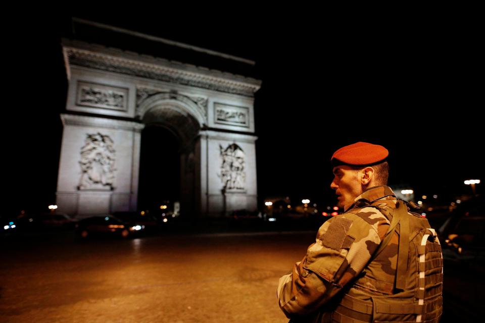  A soldier stands guard in front of the illuminated Arc De Triomphe