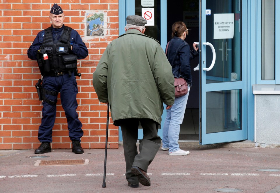 A French police officer secures a polling station as voters start to arrive for the first round of the 2017 French Presidential Election