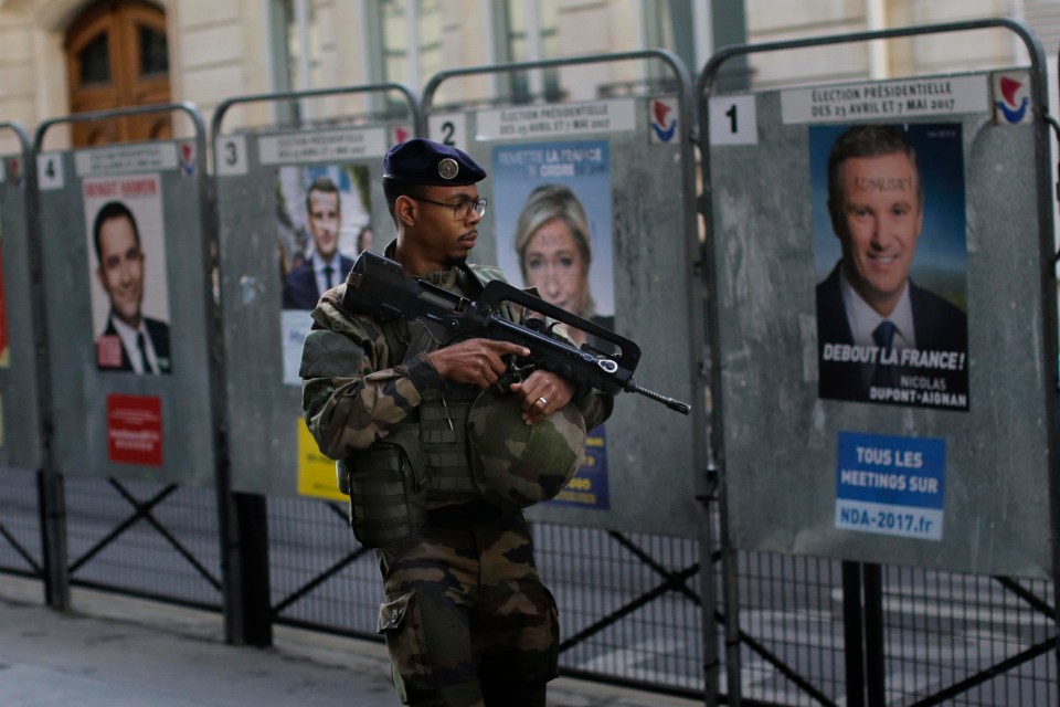 A French special forces soldier patrols past posters of the candidates