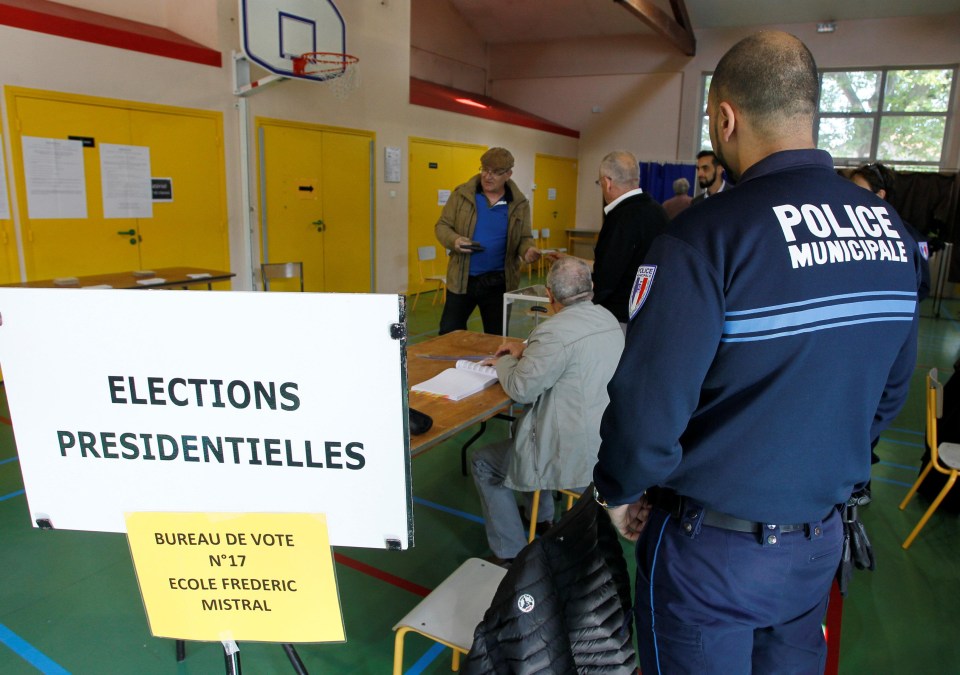 A policeman looks on as people participate in the first round of voting