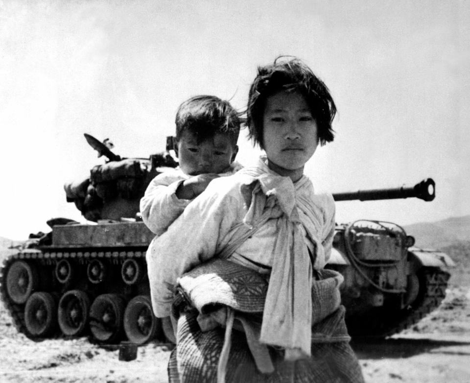  With her brother on her back a war weary Korean girl tiredly trudges by a stalled tank, at Haengju, Korea, June 9, 1951