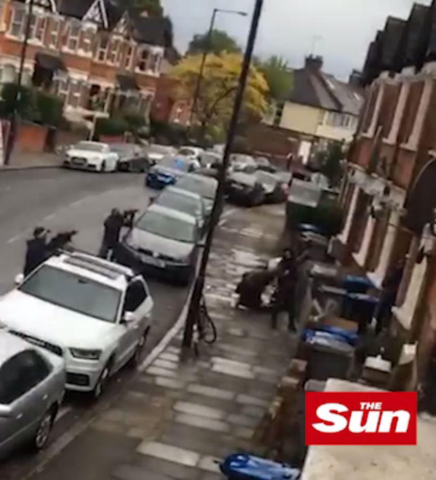  Two armed cops can be seen aiming at a house while the woman is held by officers