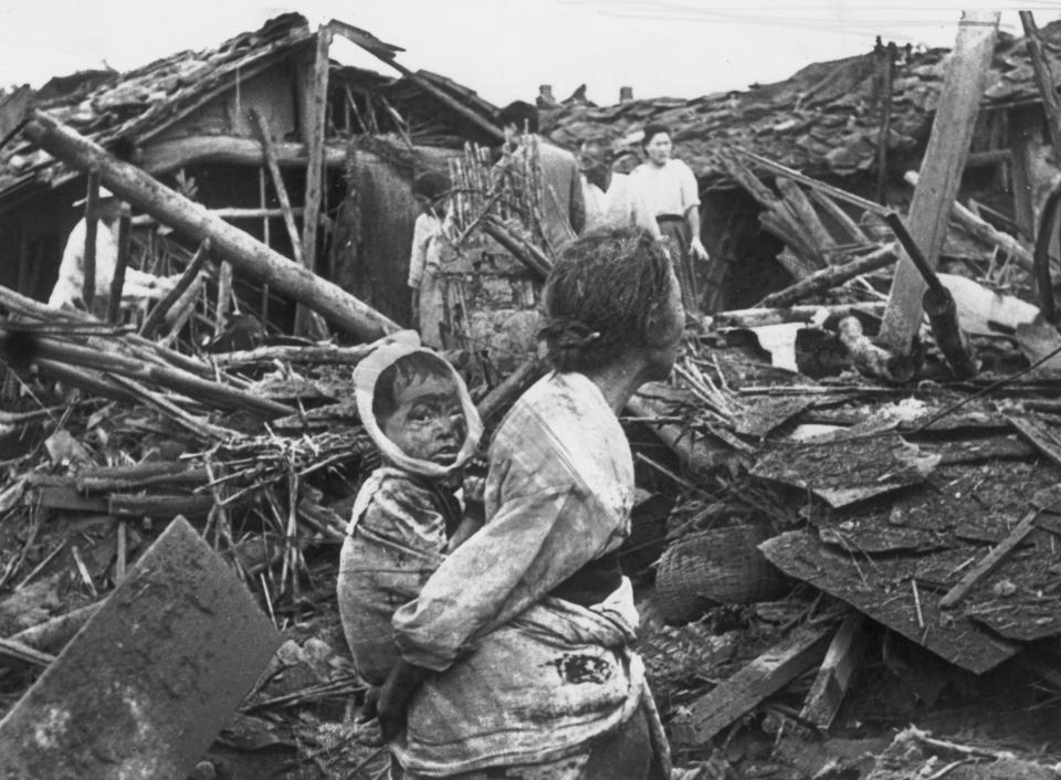  An elderly woman and her grandchild wander among the debris of their wrecked home in the aftermath of an air raid by US planes