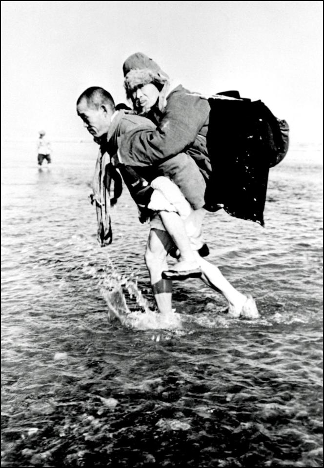  A Korean civilian carries his father on his back as they cross the Han river 30 January 1951