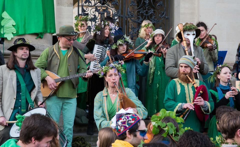  A group of musicians playing traditional instruments and adorned in green entertain crowds in Oxford