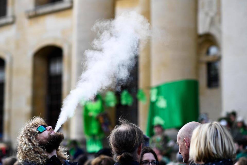  A man blows smoke into the air as thousands gathered to welcome May