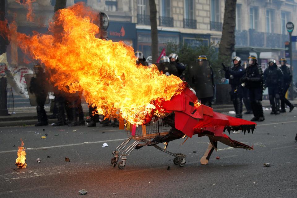  A trolley supporting a large cardboard dragon is set on fire and hurled towards police lines by protesters