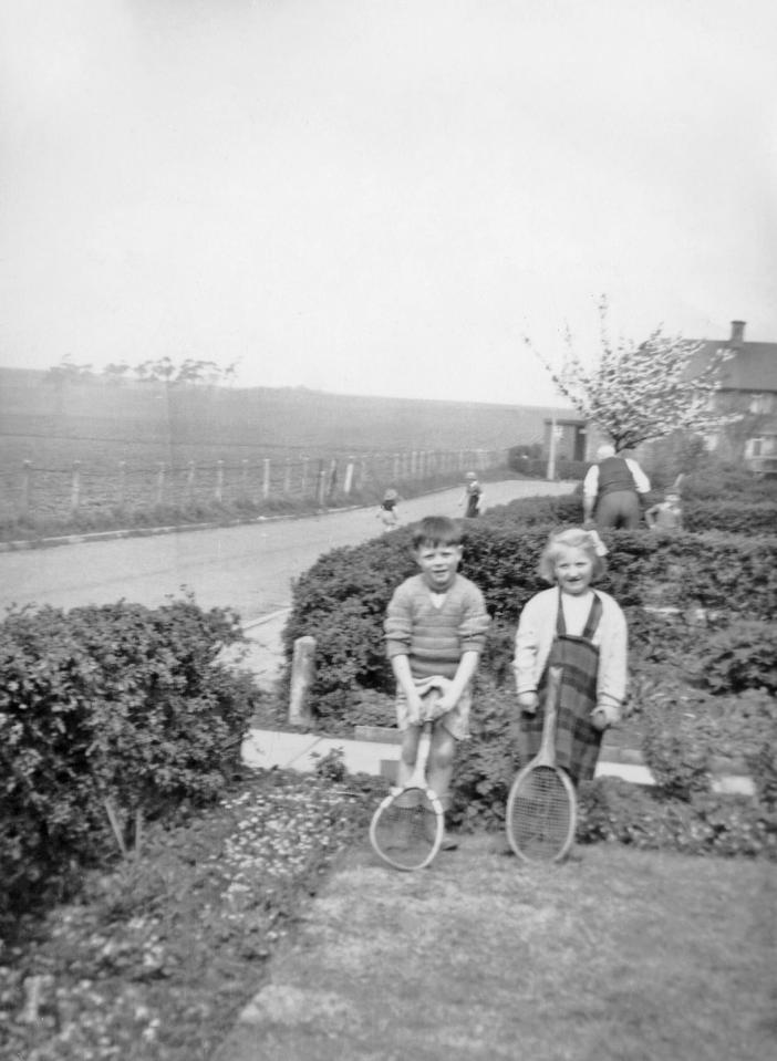  A little boy and girl sit on the garden fence with their tennis racquets after playing in the street