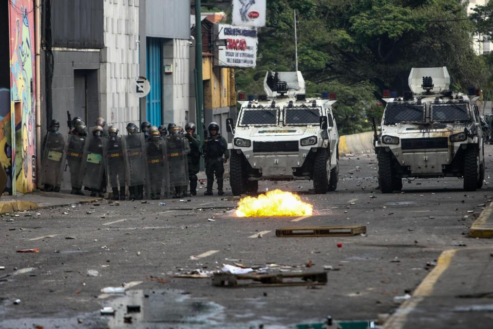  Police line up in formation next to their armoured cars as burning rubble lies ahead