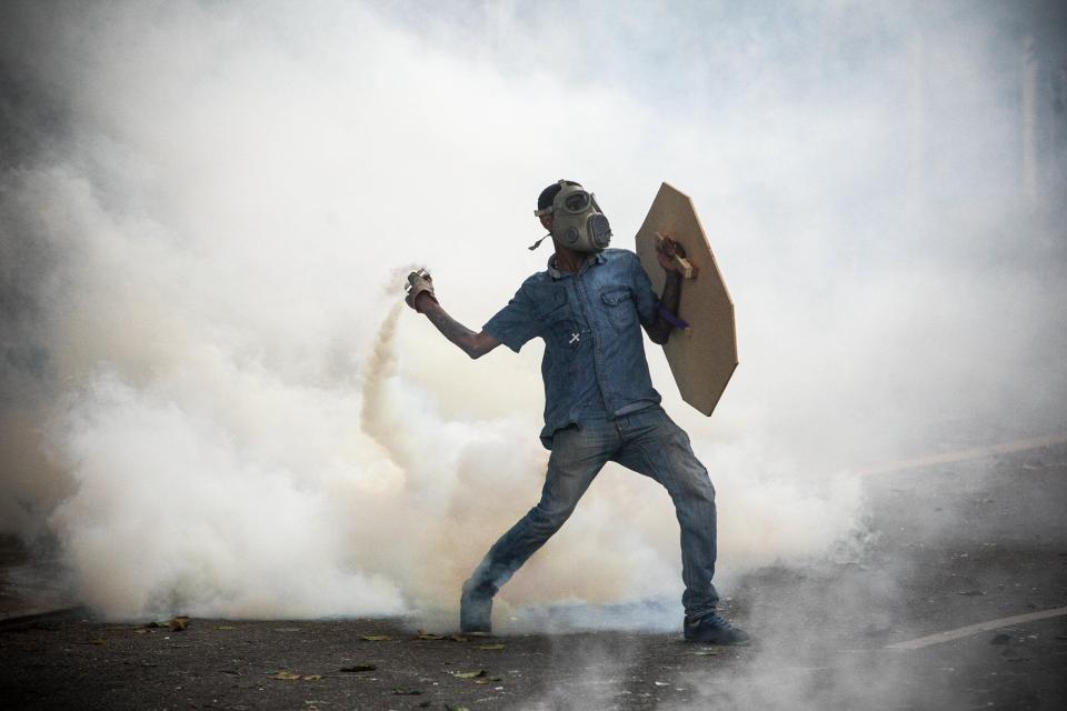  A masked protester hurls back a tear gas canister towards police lines