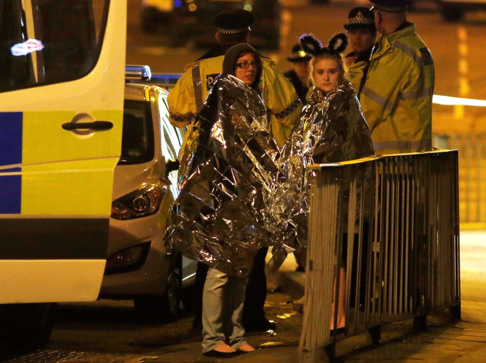 Two women wrapped in thermal blankets stand near the Manchester Arena