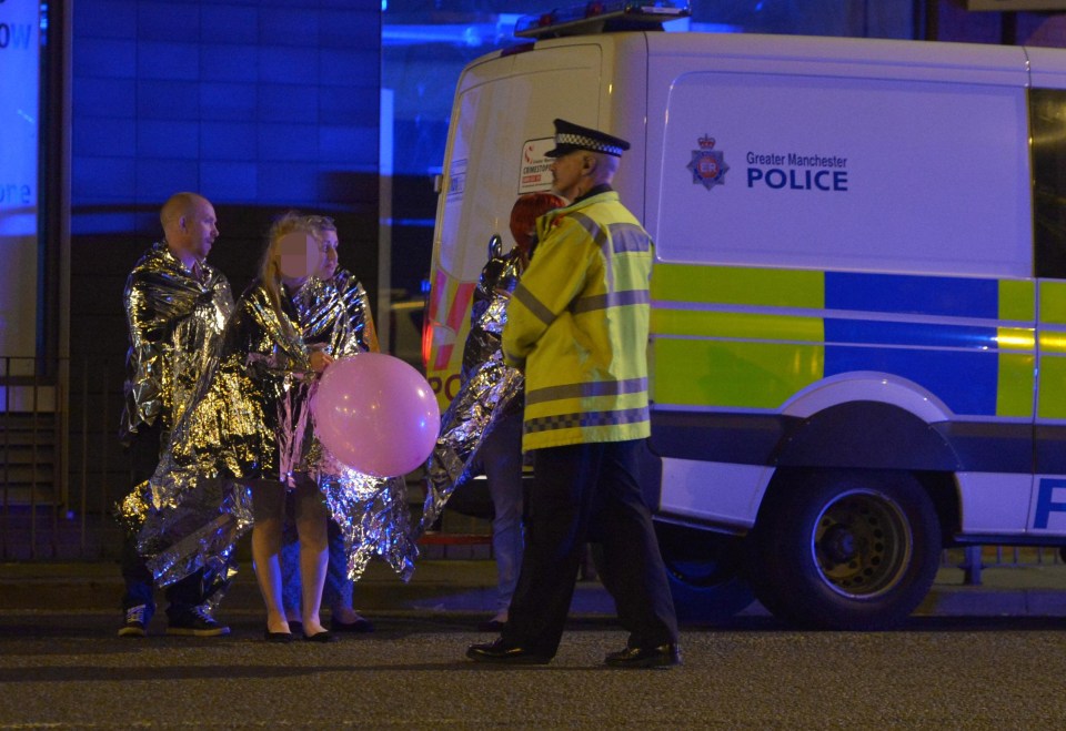 Stranded concert-goers wrapped in thermal blankets wait by police van after bombing