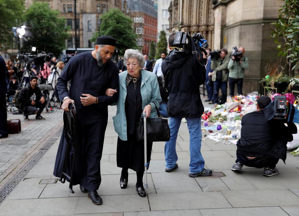  Muslim man Sadiq Patel and elderly Jewish woman Renee Rachel Black walk by floral tributes in Albert Square in Manchester