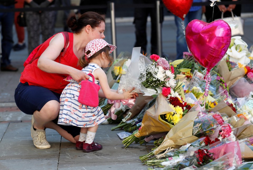 A woman helps a young girl place flowers in the square