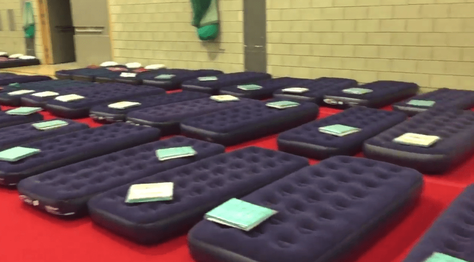 The footage shows dozens of inflatable beds packed side-by-side on the gym floor