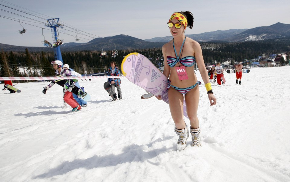 A woman climbs up a mountain carrying her snowboard enjoying the hot weather