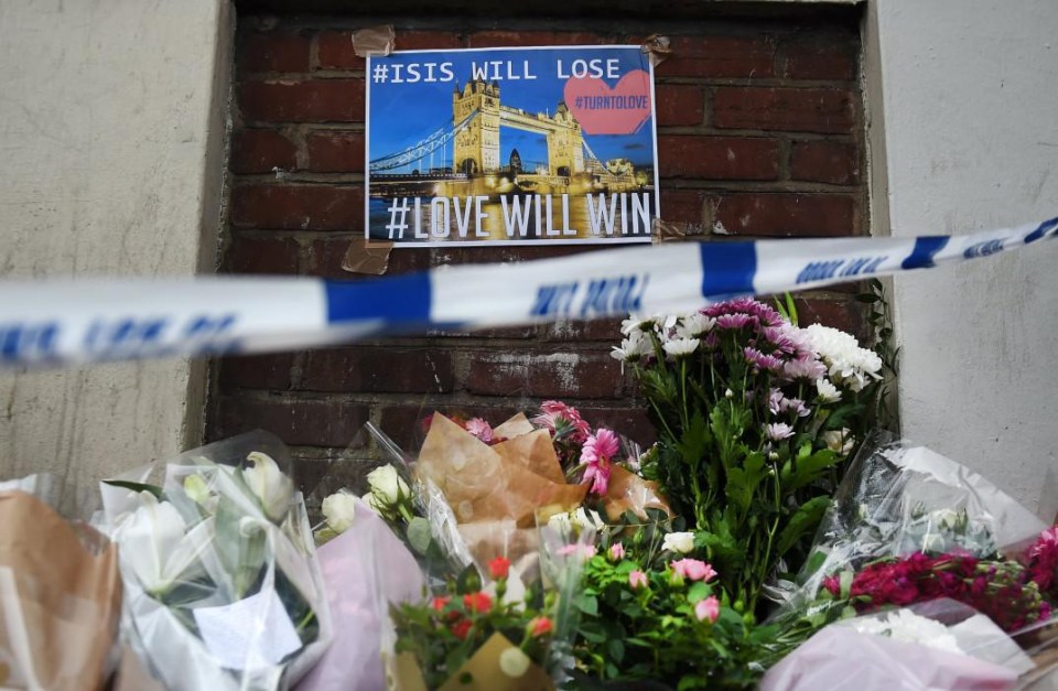 People have laid flowers under a a poster declaring ‘ISIS will lose’ and ‘Love will win’