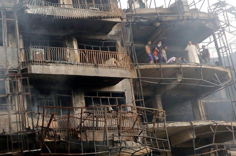  Iraqis look on as they inspect the site of suicide car bomb attack in the Karada district of central Baghdad