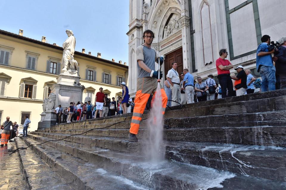  Tourists look on as a cleaner covers the church steps in water