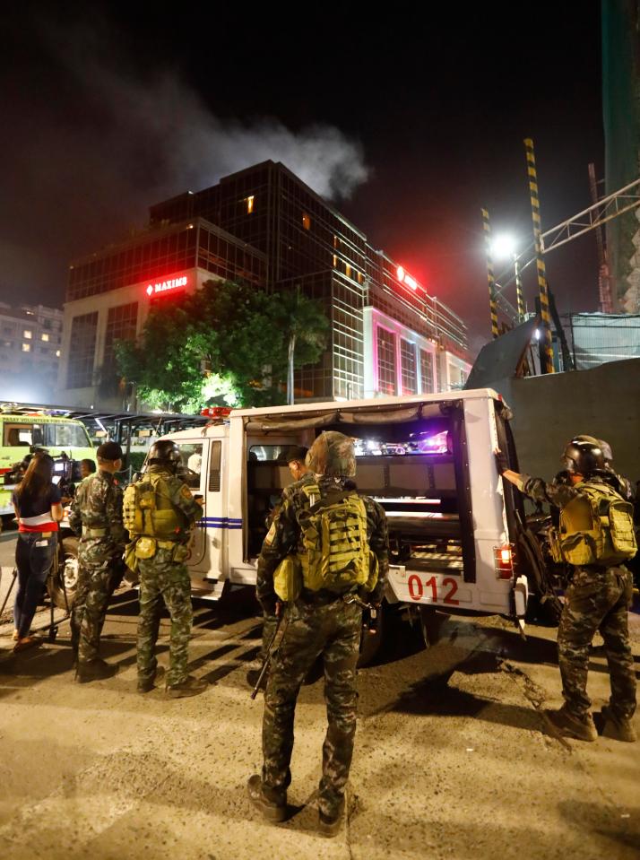  Smoke rises from the The Resorts World Manila hotel and casino complex as police maintain security