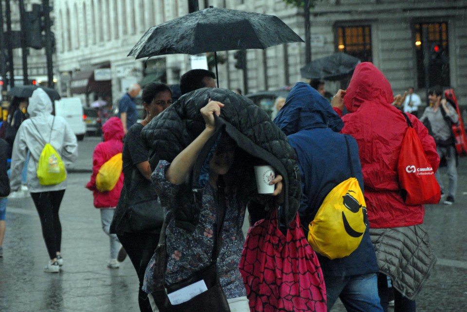 People in Trafalgar Square in London try and shield themselves from the heavy rain this afternoon