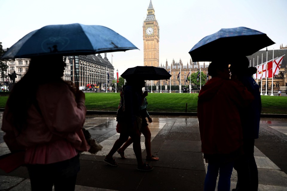 People shelter under umbrellas during afternoon rain showers in Westminster