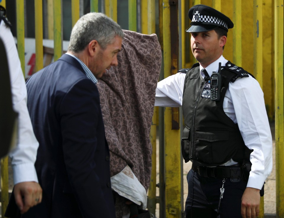 Police officers escort a person detained after a property was raided in Barking, east London