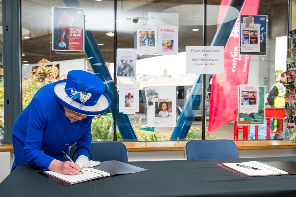  The Queen signed a book of condolence with posters pleading for information about the missing on a window behind her