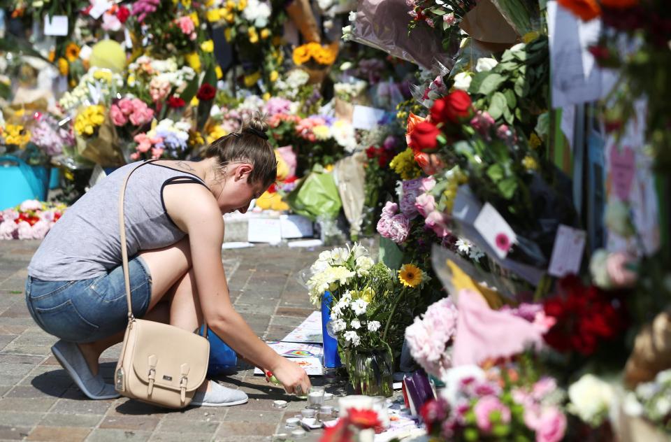  A woman places a tribute next to the flowers and cards amassed at the site