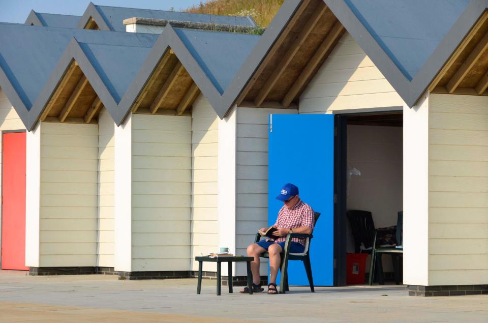  A man takes things easy outside his beach hut at the seaside resort of Swanage in Dorset on a morning of warm hazy sunshine