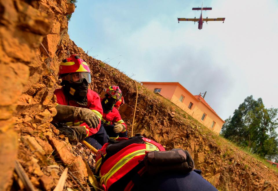  Some firefighters protect themselves as a Canadair firefighting plane drops its load on a wildfire in Vale da Ponte