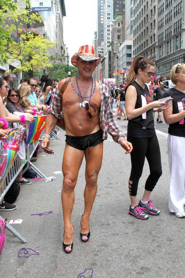 A marcher shows off his physique while wearing a cowboy hat and high heels