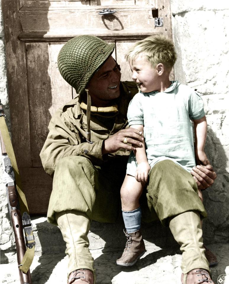  1944: U.S. Army Pfc. Fred Linden of Detroit, Michigan, 38th Infantry Regiment, 2nd Infantry Division, holds a young French boy following the liberation of the village of Trévières during the Battle of Normandy.