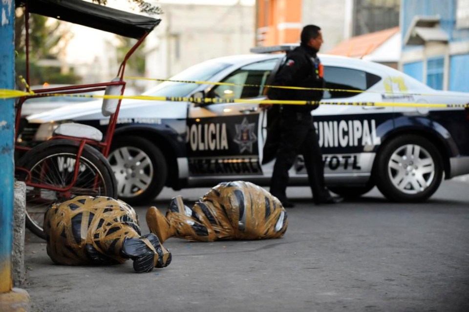 A cop walks past two dead bodies wrapped in plastic and sticky tape in Mexico City 