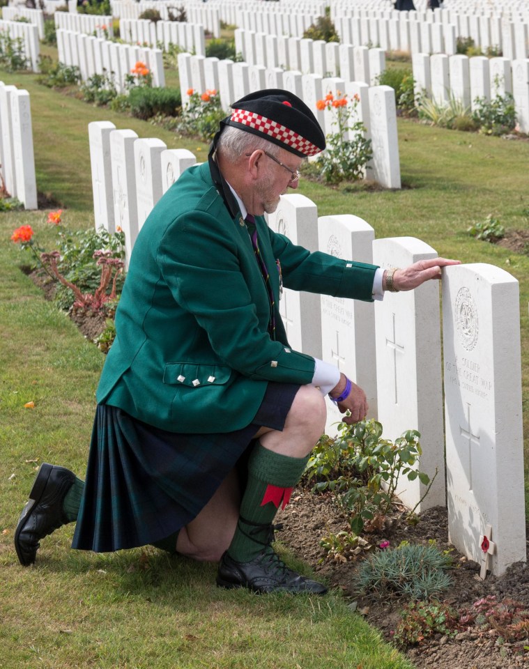 A soldier kneels before a grave at Tyne Cot today