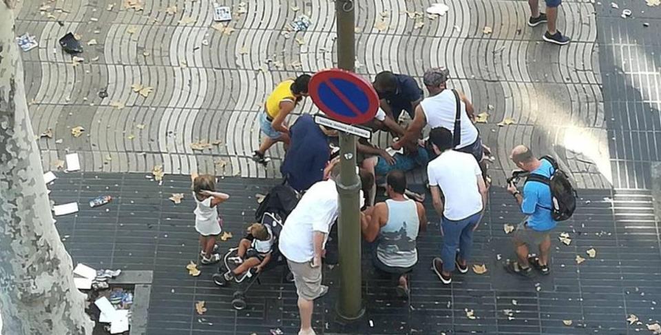  A small crowd of people tend to an injured person on the ground following the terror attack in Las Ramblas