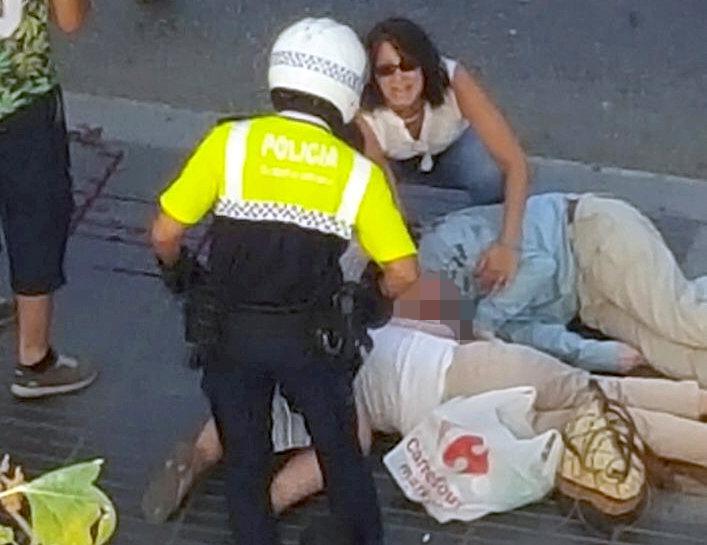  A woman talks to a Spanish cop as two people lay on the ground after the horrifying terror attack