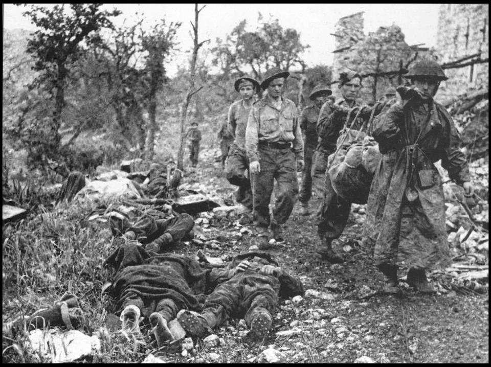  Polish infantrymen carry a wounded comrade past dead German defenders