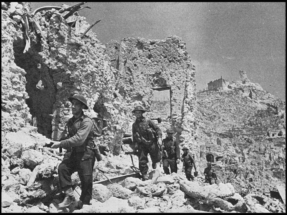  Men of the 2nd NZ Infantry Division advance into the town past the ruins of the Hotel Des Roses