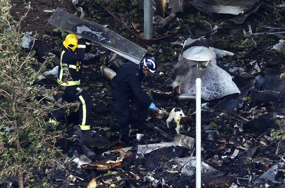 Firefighters and sniffer dogs search through the debris at the foot of Grenfell Tower 