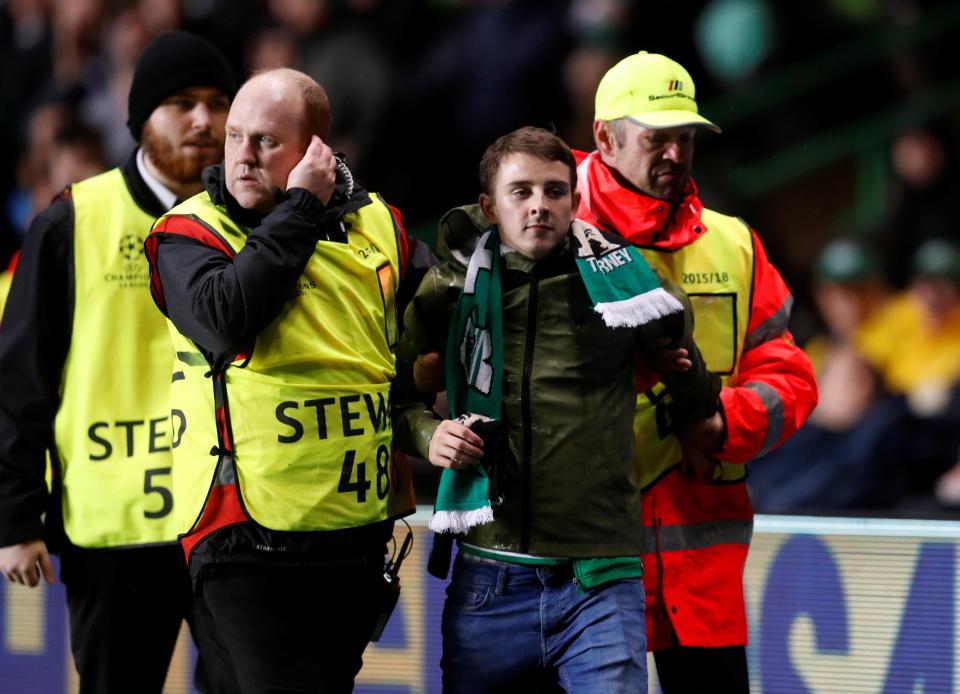  A Celtic fan is carted away after breaking onto the pitch to aim a kick at Kylian Mbappe