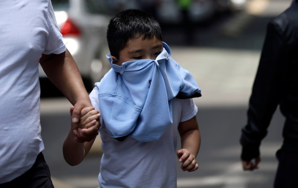 A child clasps the hand of an adult while being led to safety with his face covered 