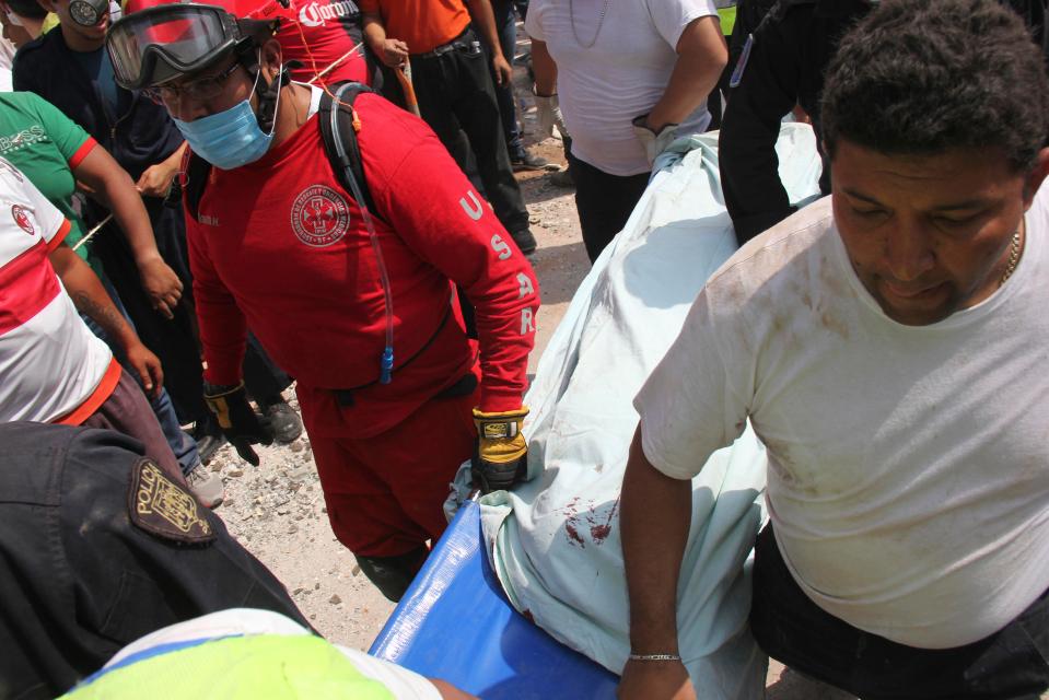  Rescuers carry a stretcher through the crowds as they remove those trapped from the school rubble