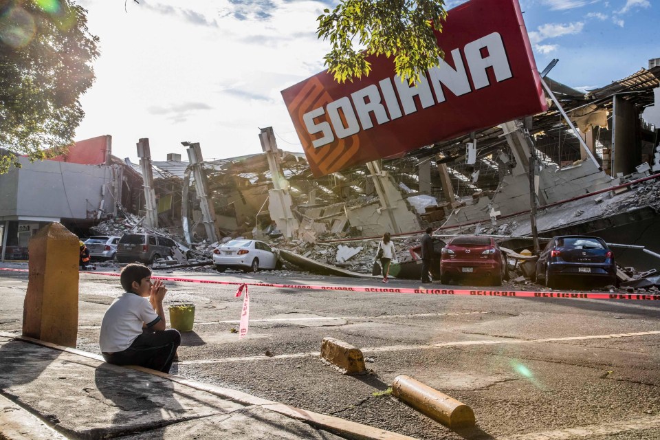 A boy sits in the gutter as he stares at the destruction in Mexico City