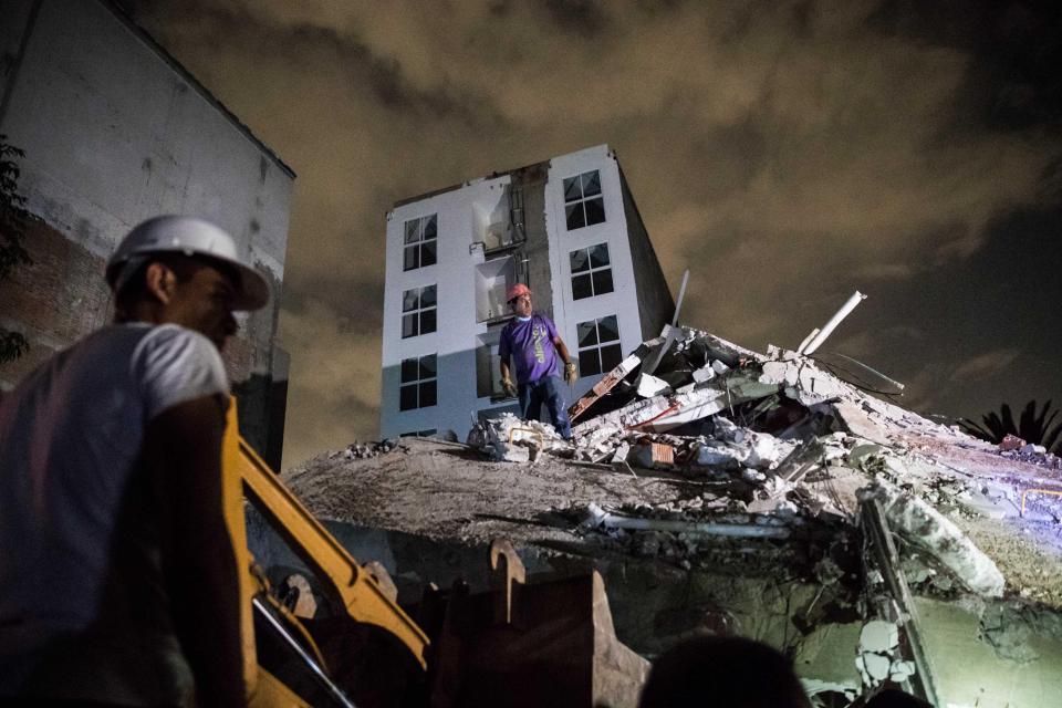  A man stands on a pile of rubble during the overnight searches