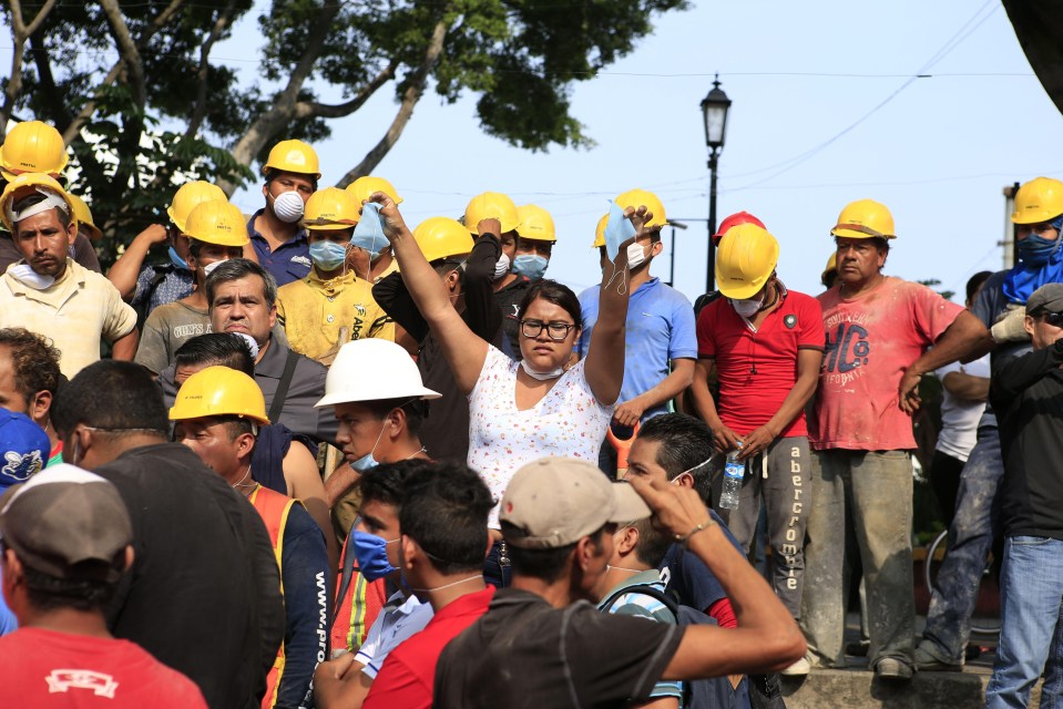 A woman dishes out masks in front of a collapsed building 