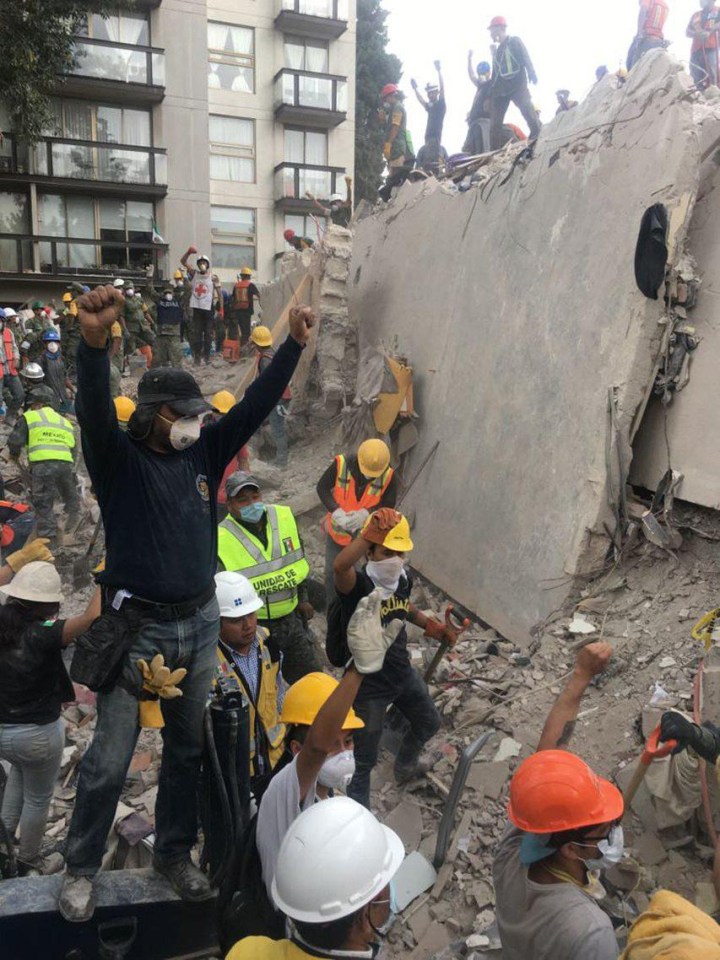 Police raise their hands as a sign of a request for absolute silence, after hearing some noise during the search for people still alive