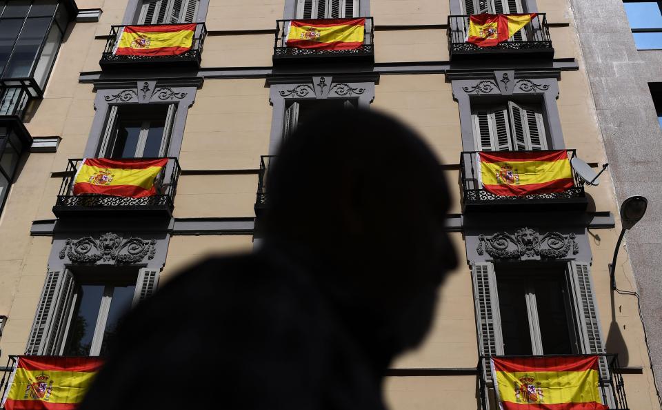  A man walks past a building with Spanish flags hanging from the balconies in Madrid