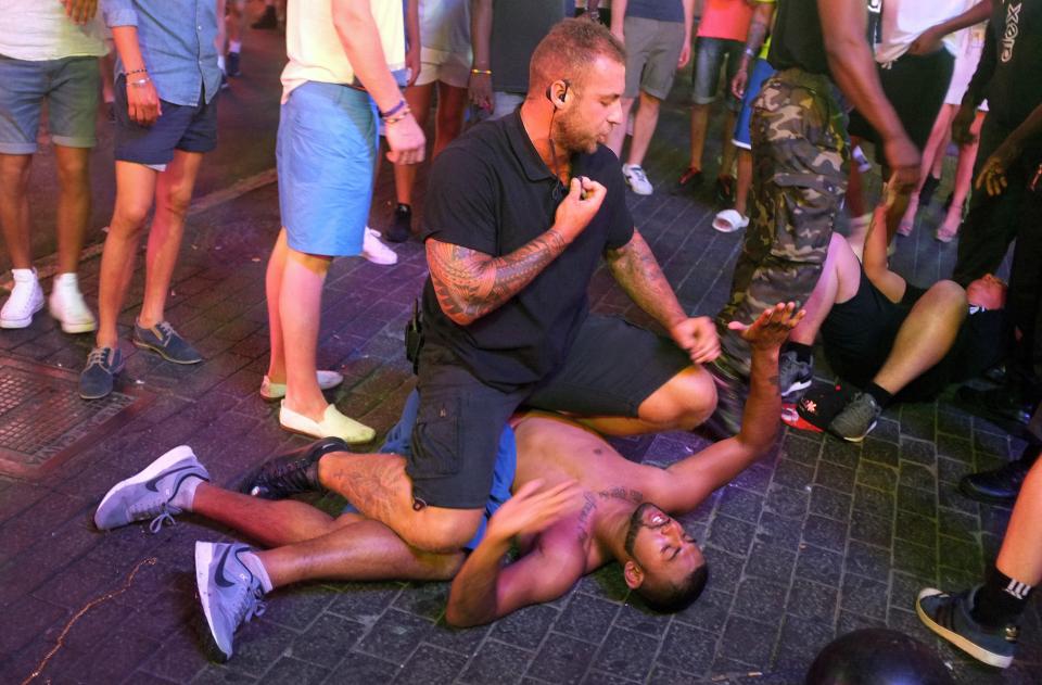  A bouncer sits on top of a young reveller who holds his hands up in Magaluf